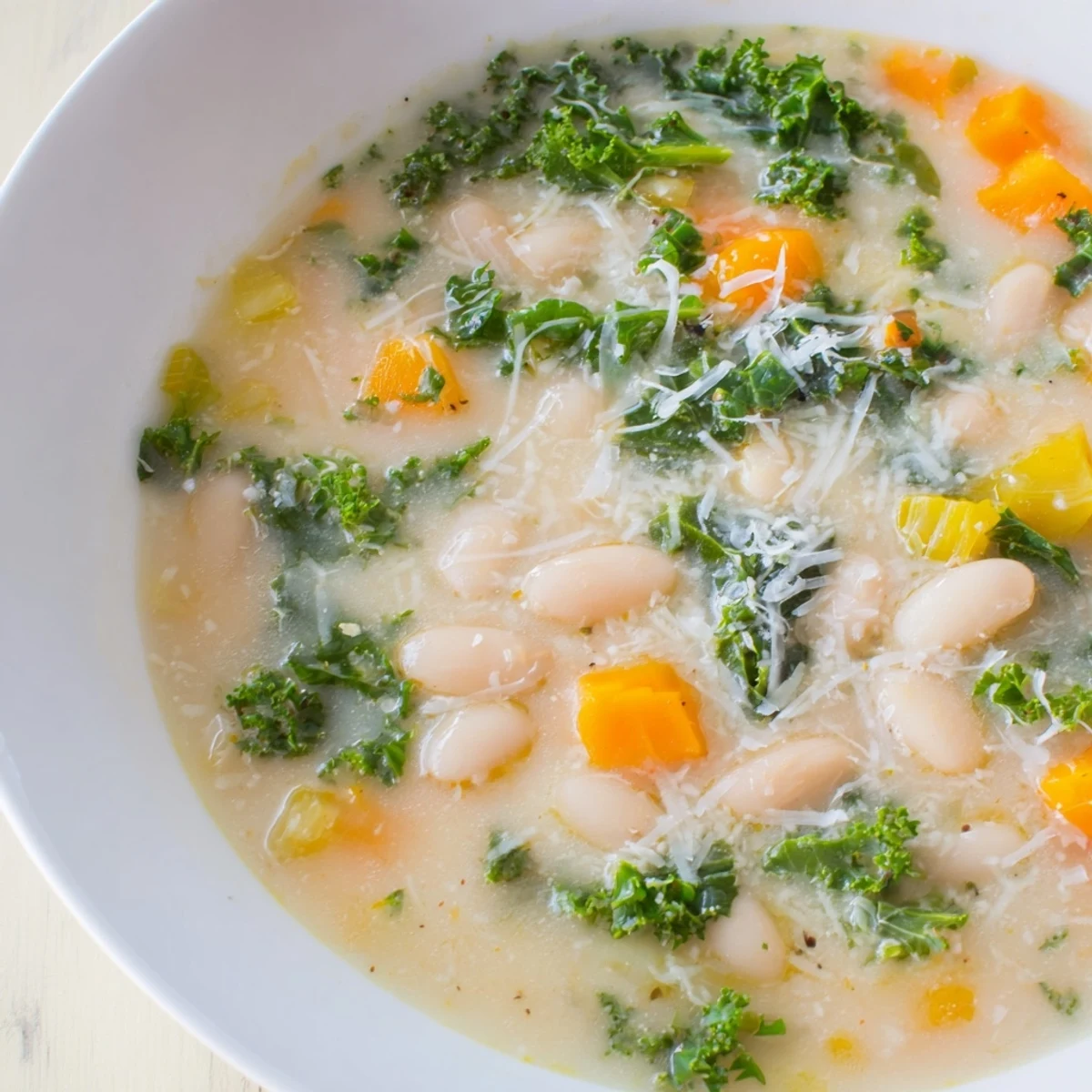 A steaming bowl of Creamy White Bean and Kale Soup, garnished with Parmesan cheese and ready to eat.