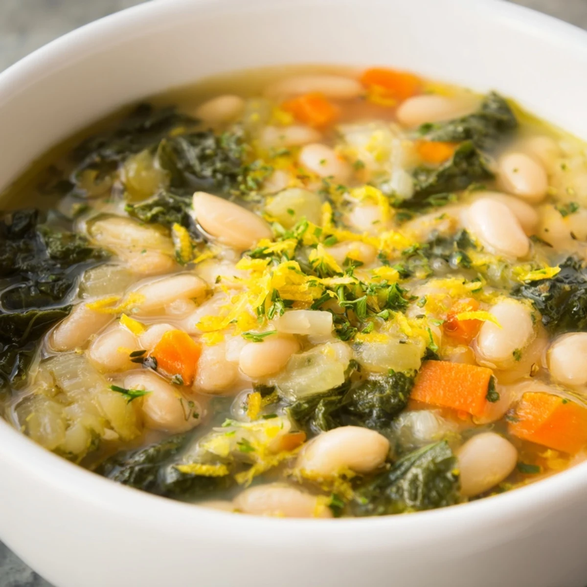 Healthy White Bean and Kale Soup with Lemon Zest is ready to eat, showcasing vibrant greens and golden olive oil swirls.