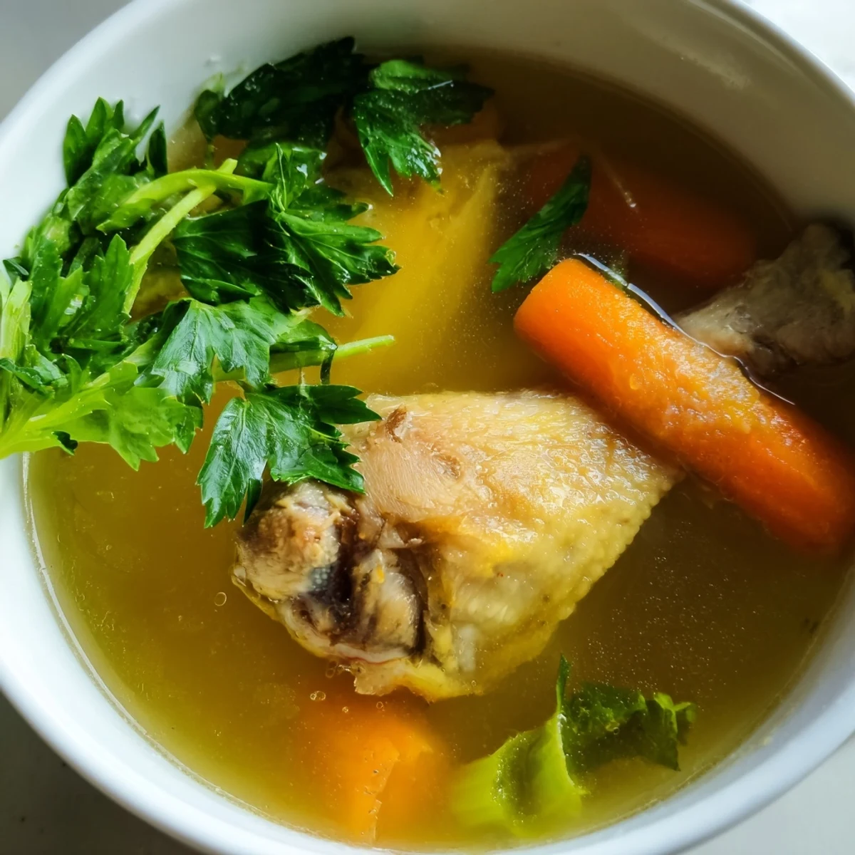 Steaming bowl of golden Homemade Chicken Bone Broth with Ginger and aromatic herbs.