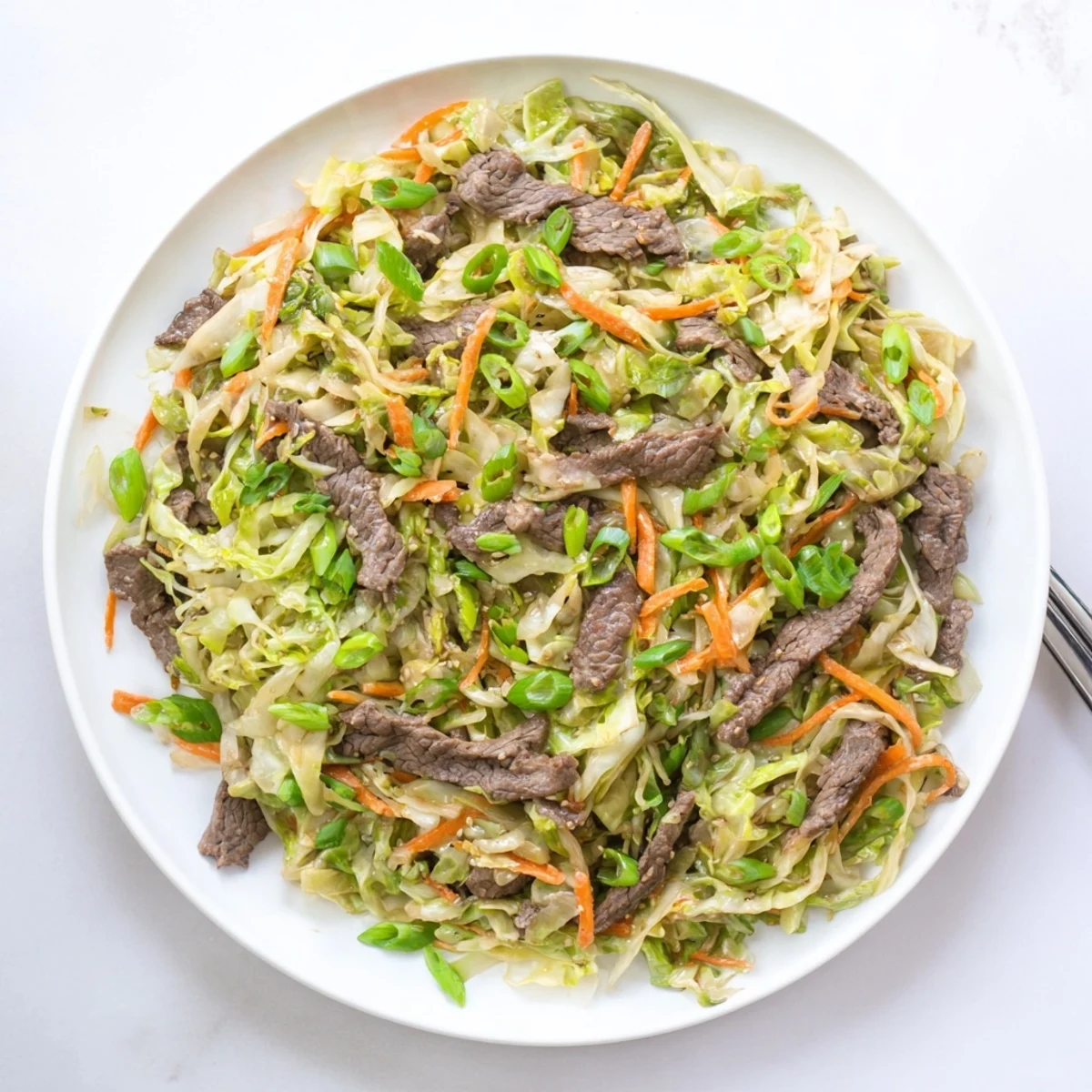 Sizzling Keto Friendly Beef and Cabbage Stir Fry in a skillet, garnished with sesame seeds and chili flakes.