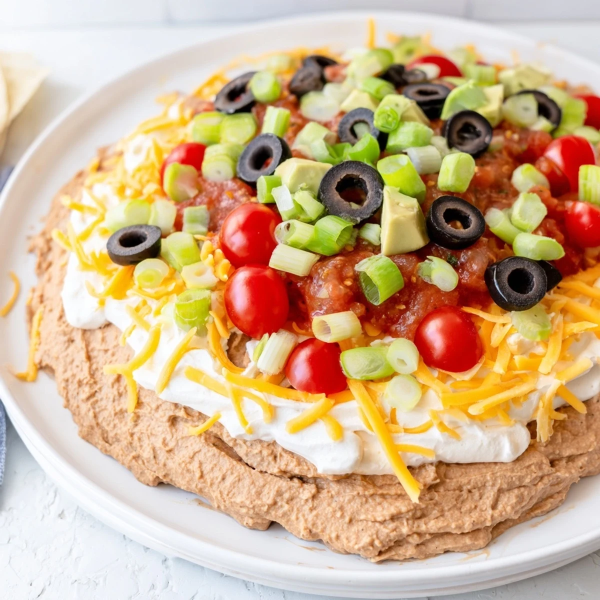 A close-up of Ultimate Layered Taco Dip, featuring creamy cheese, vibrant salsa, and fresh avocado, with a side of chips.