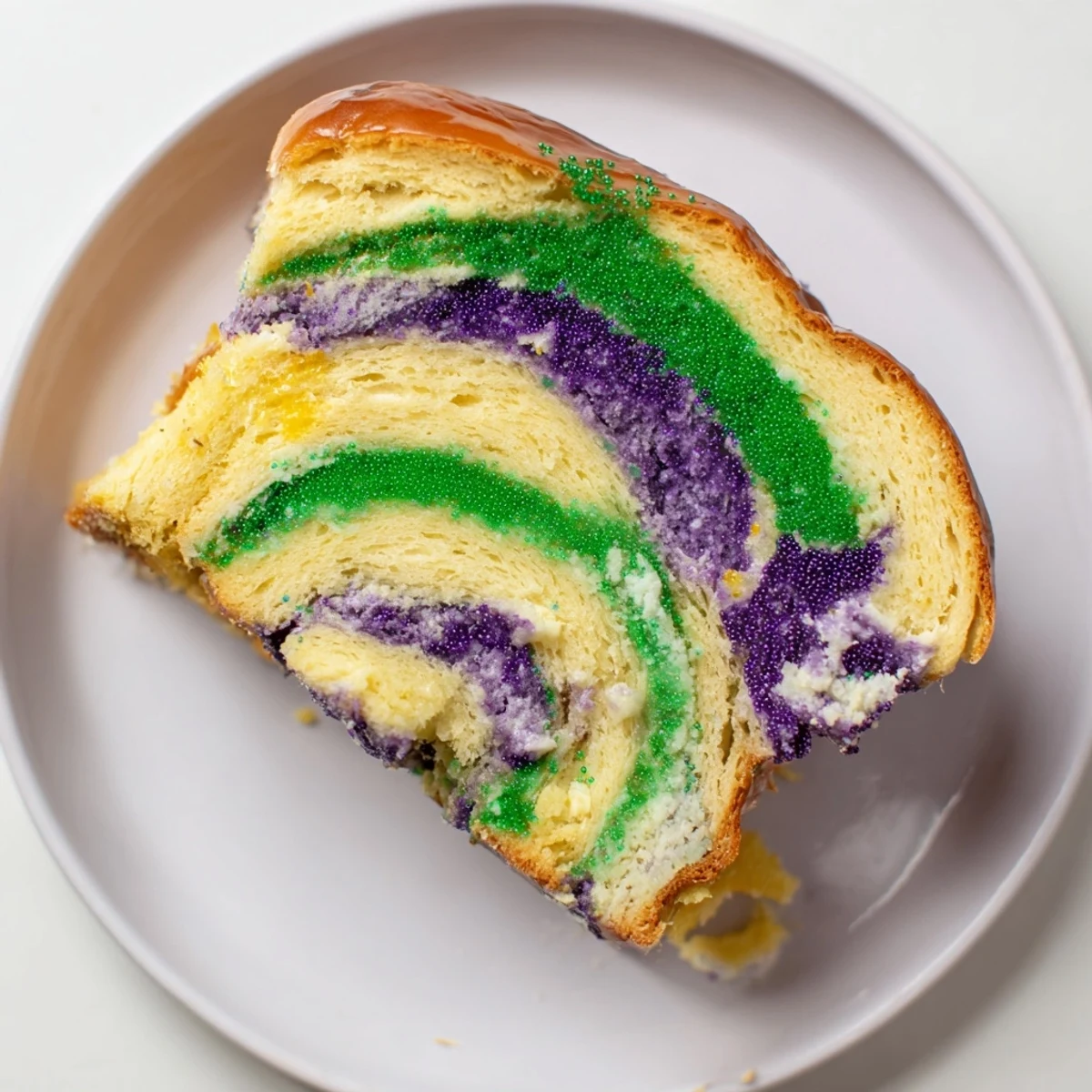 Traditional New Orleans King Cake dusted with sparkling colored sugars and sweet cream cheese frosting.