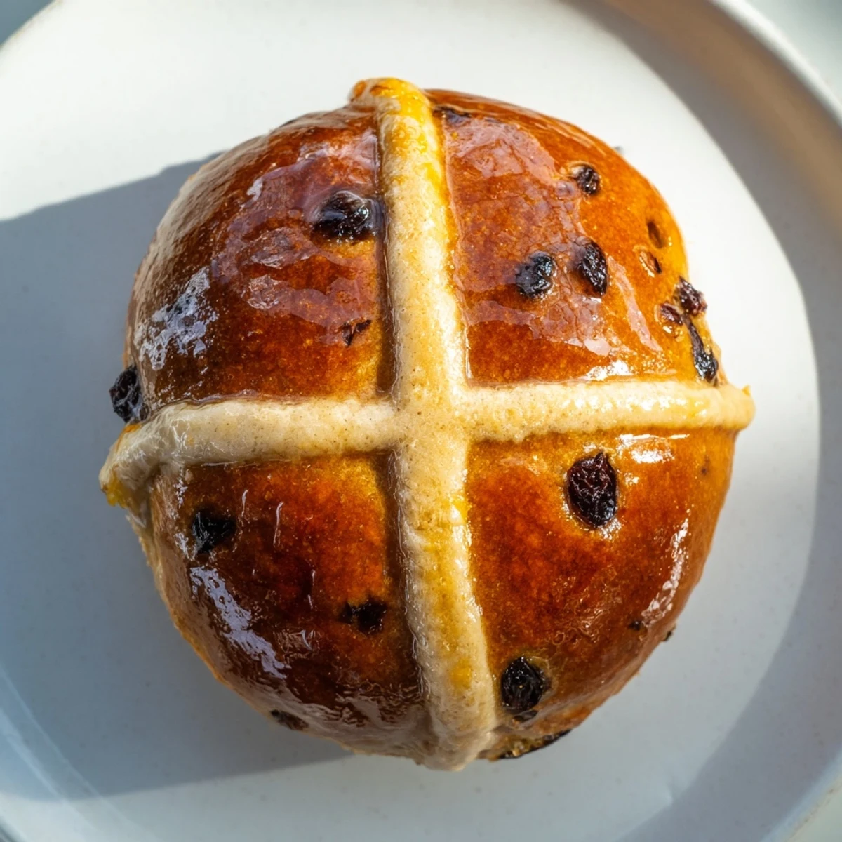 Twelve golden hot cross buns with currants and spices, fresh from the oven, glistening with apricot glaze on a wire rack.  