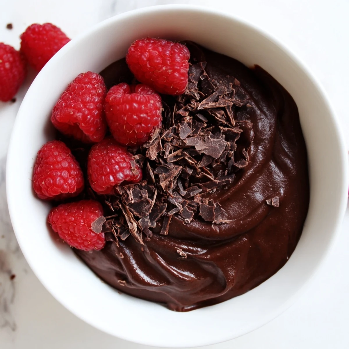 Silky Dark Chocolate Avocado Mousse with Raspberries showing chocolate shavings and fresh fruit on a marble countertop.