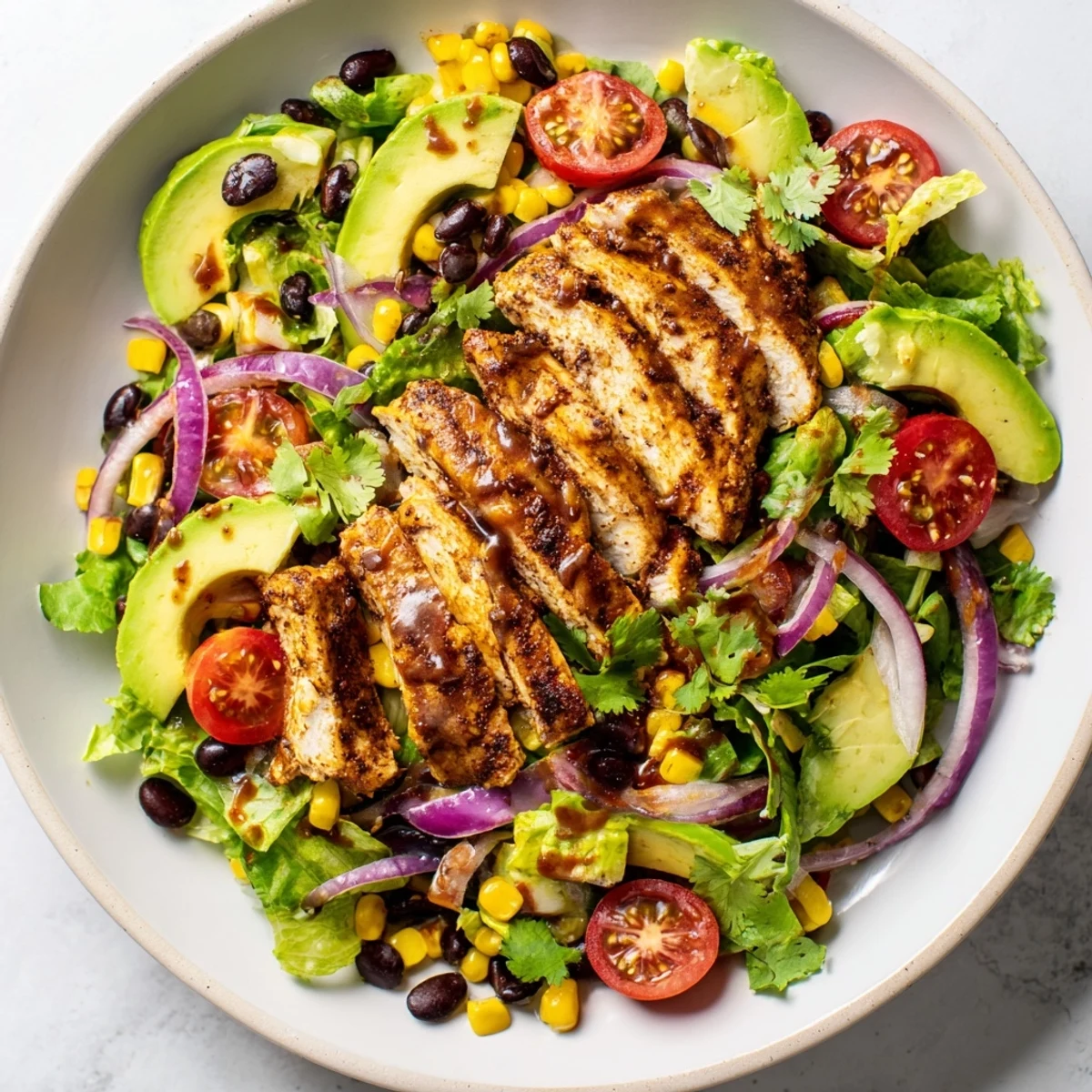 A vibrant photo of Chipotle Lime Chicken Salad with grilled sliced chicken, black beans, corn, avocado, and lime dressing on greens. 