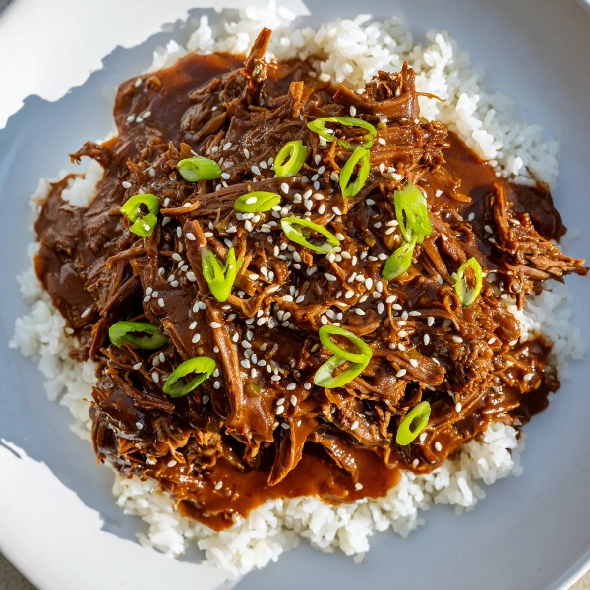 Shredded Crock Pot Korean Beef piled high over fluffy jasmine rice with green onions.