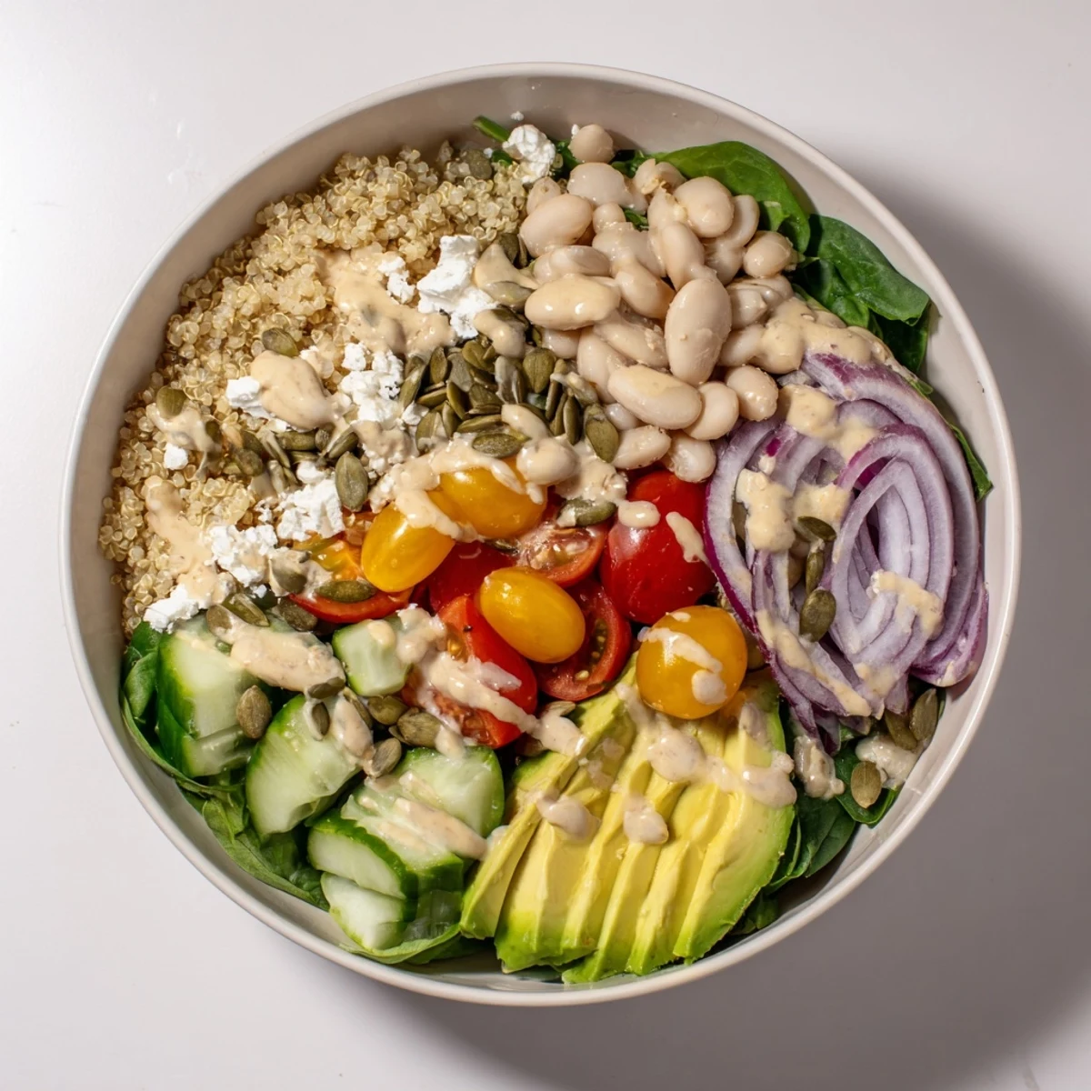 Vibrant Spinach & White Bean Ultimate Protein Power Bowl topped with creamy avocado and toasted pepitas, drizzled with tangy lemon tahini dressing.