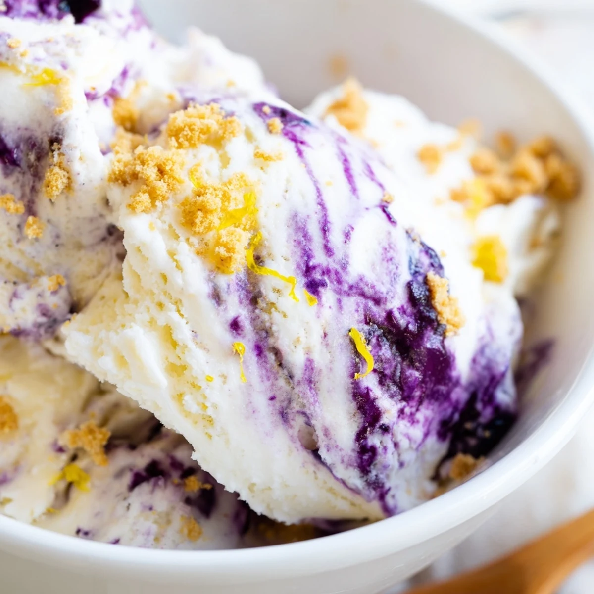 A scoop of Lemon Blueberry Cheesecake Ice Cream in a waffle cone, showing creamy texture and vibrant berry swirls.