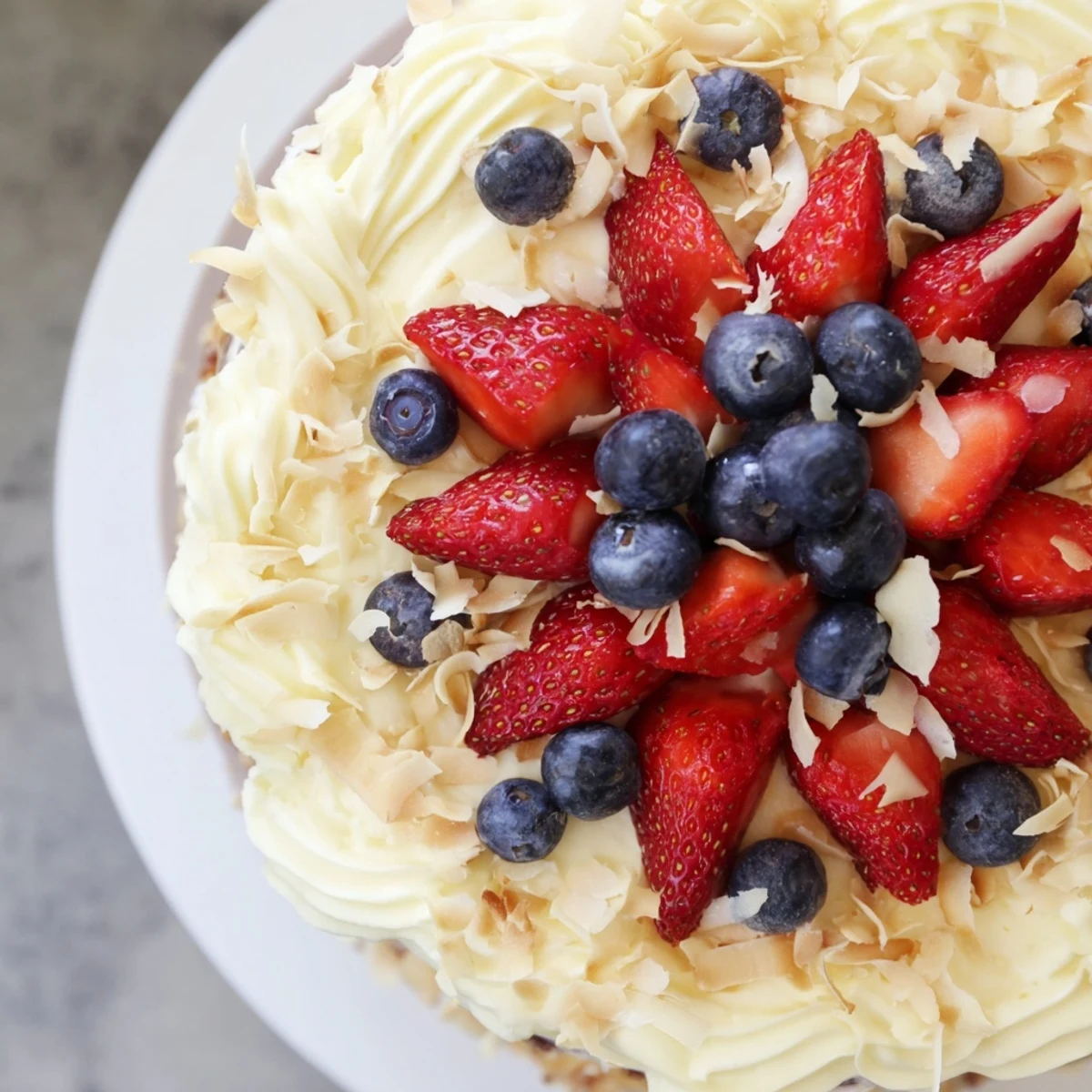 Moist Pineapple Coconut God Bless America Cake decorated with strawberries, blueberries, and sweet coconut flakes.