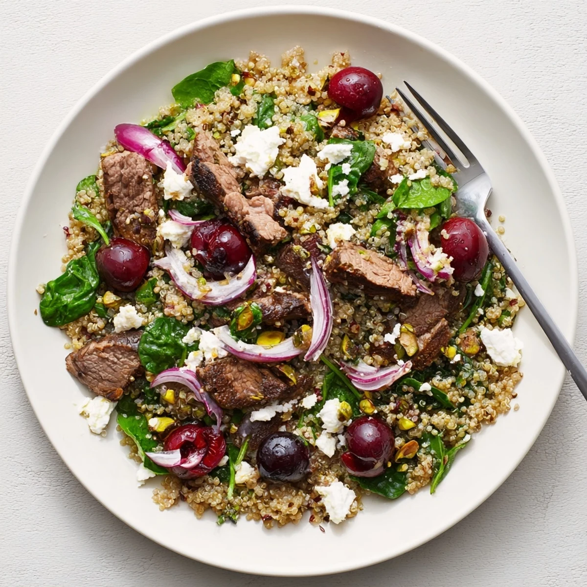 Colorful cherry quinoa salad with lamb topped with feta, pistachios, and fresh herbs