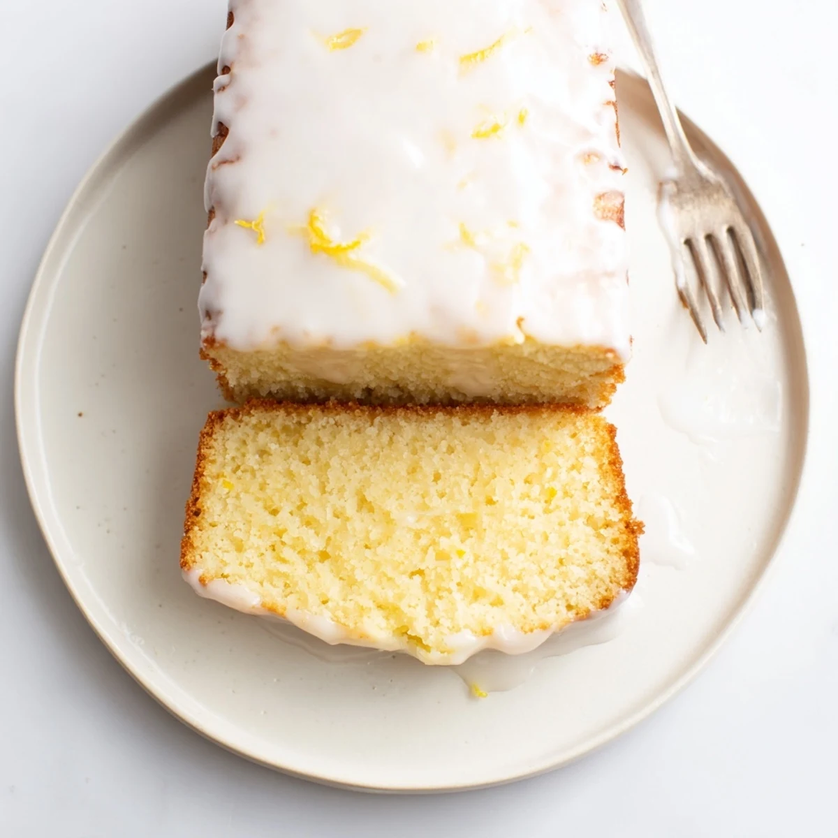 Golden slice of bright lemon loaf cake drizzled with tangy citrus glaze on a white plate