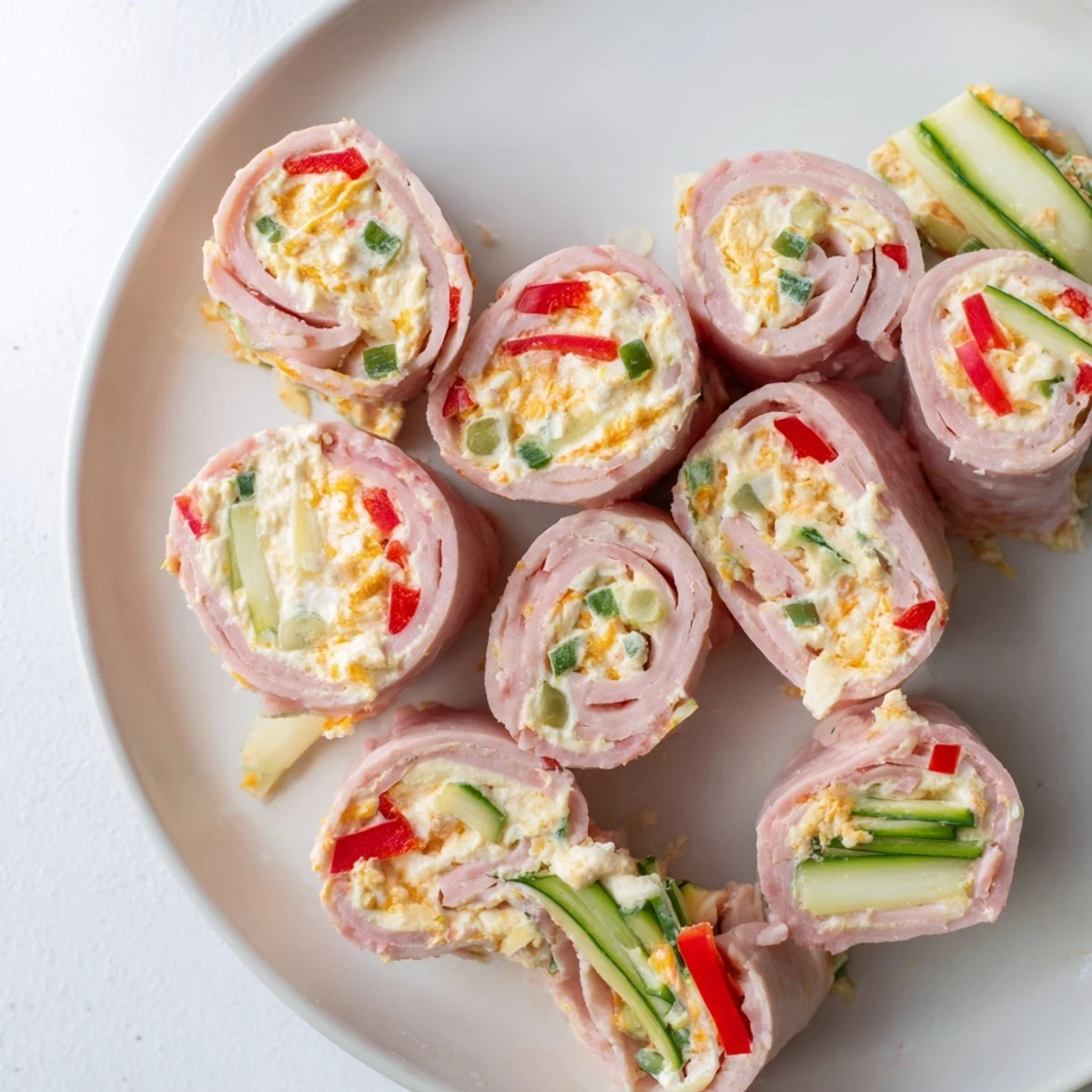 Golden keto ham roll ups featuring spiraled deli ham wrapped around creamy cheddar cheese filling and crisp colorful vegetable strips