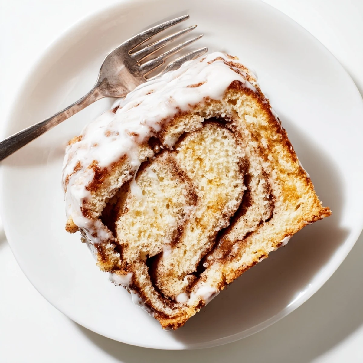 Warm breakfast cinnamon roll cake with swirled cinnamon sugar pockets and silky glaze on a serving plate