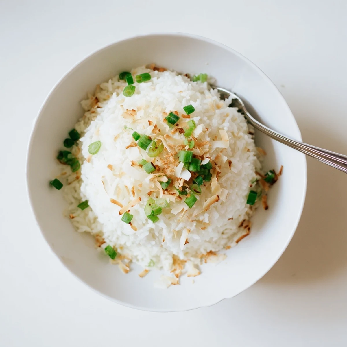 Creamy white coconut rice fluffed with a fork and topped with green scallions
