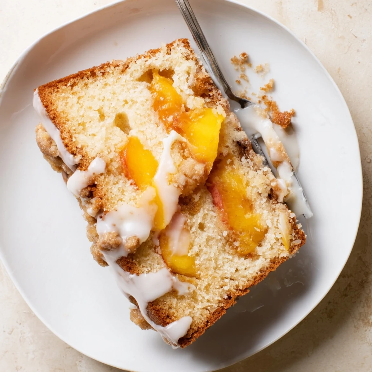 Golden peach cobbler pound cake drizzled with vanilla glaze on serving plate