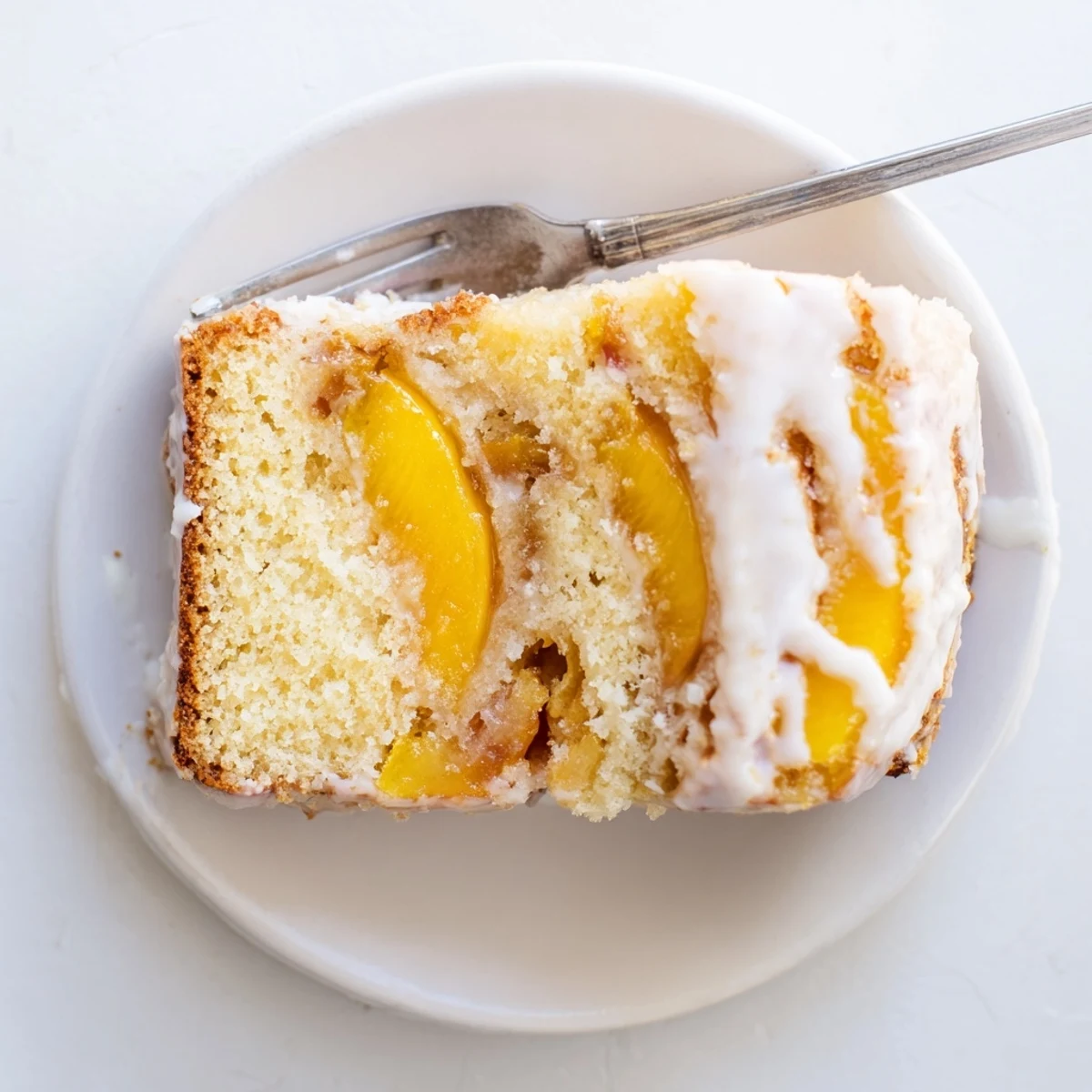 Rich peach cobbler pound cake slice showing juicy fruit and glaze texture