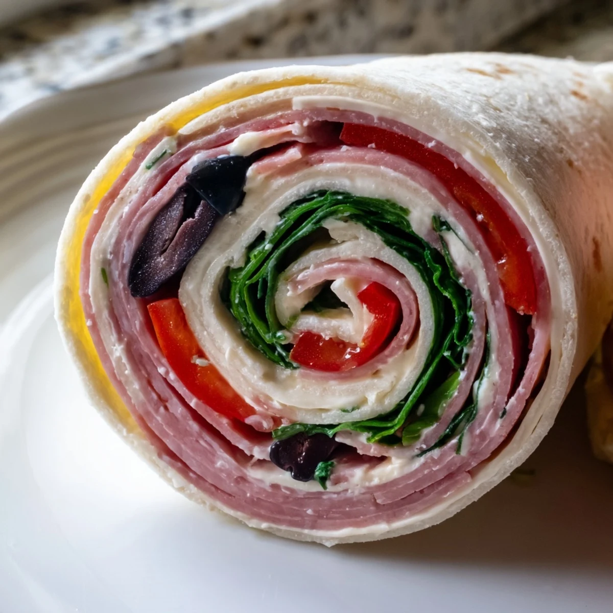Bite-sized Italian pinwheel sandwiches arranged on a board, revealing spiral layers of ham, pepperoni, cream cheese, and crisp vegetables