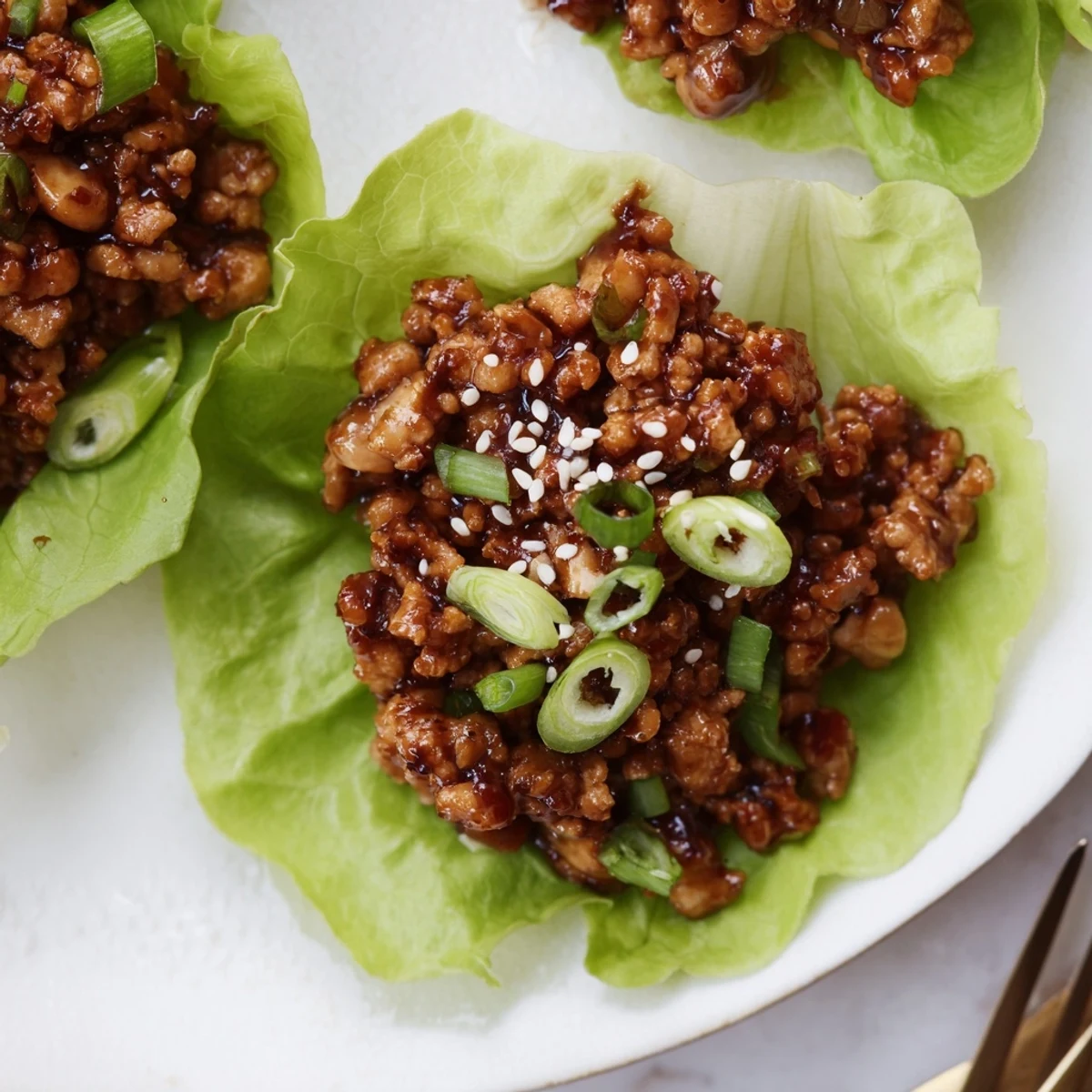 Golden brown chicken lettuce wraps garnished with green onions and sesame seeds on white plate