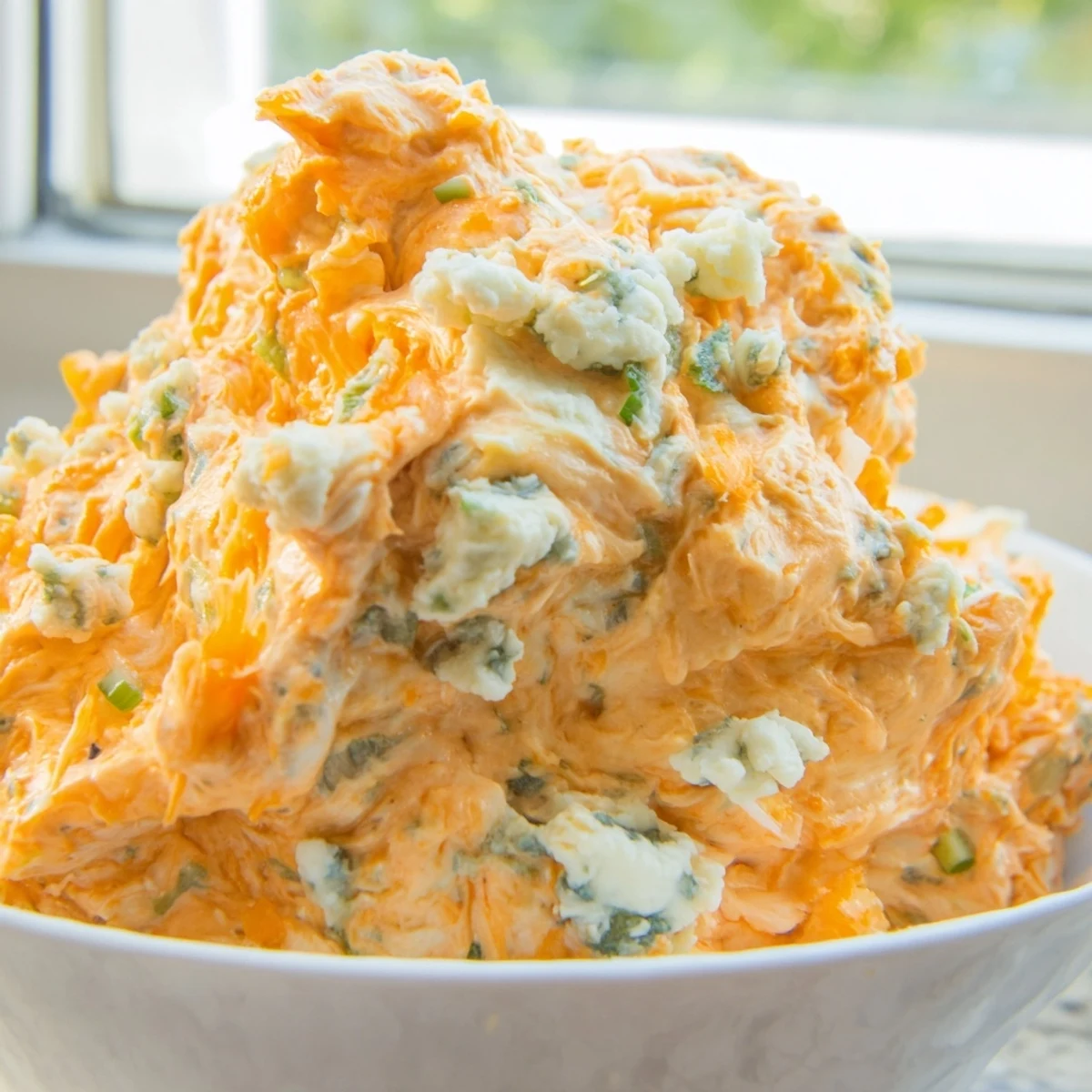 Creamy buffalo pickle dip in a serving bowl surrounded by crunchy chips and fresh veggie sticks